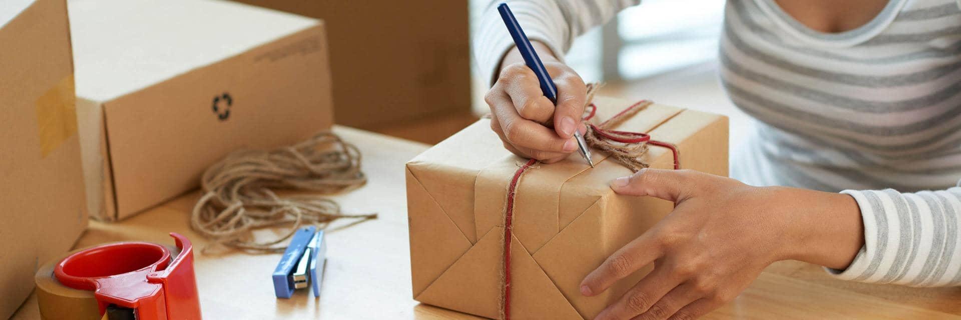 A woman writes an address on a hand wrapped brown paper parcel tied with string